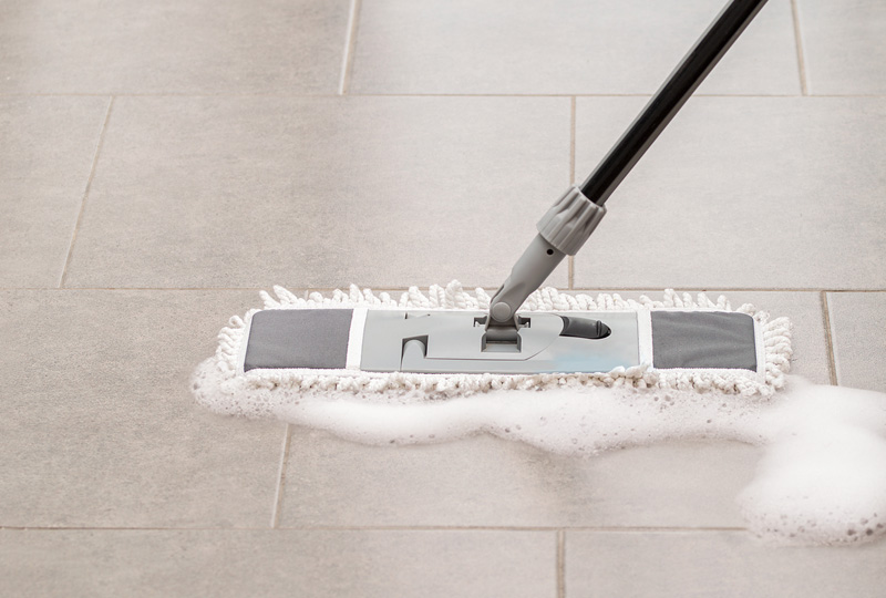 Man cleaning a set of stone-effect porcelain floor tiles using a squeeze mop
